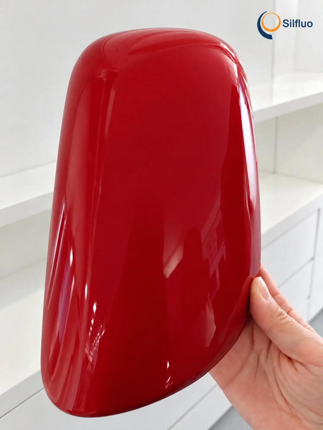 Hand holding a curved automotive-style panel in deep red high gloss finished with a transparent polysilazane clear coat