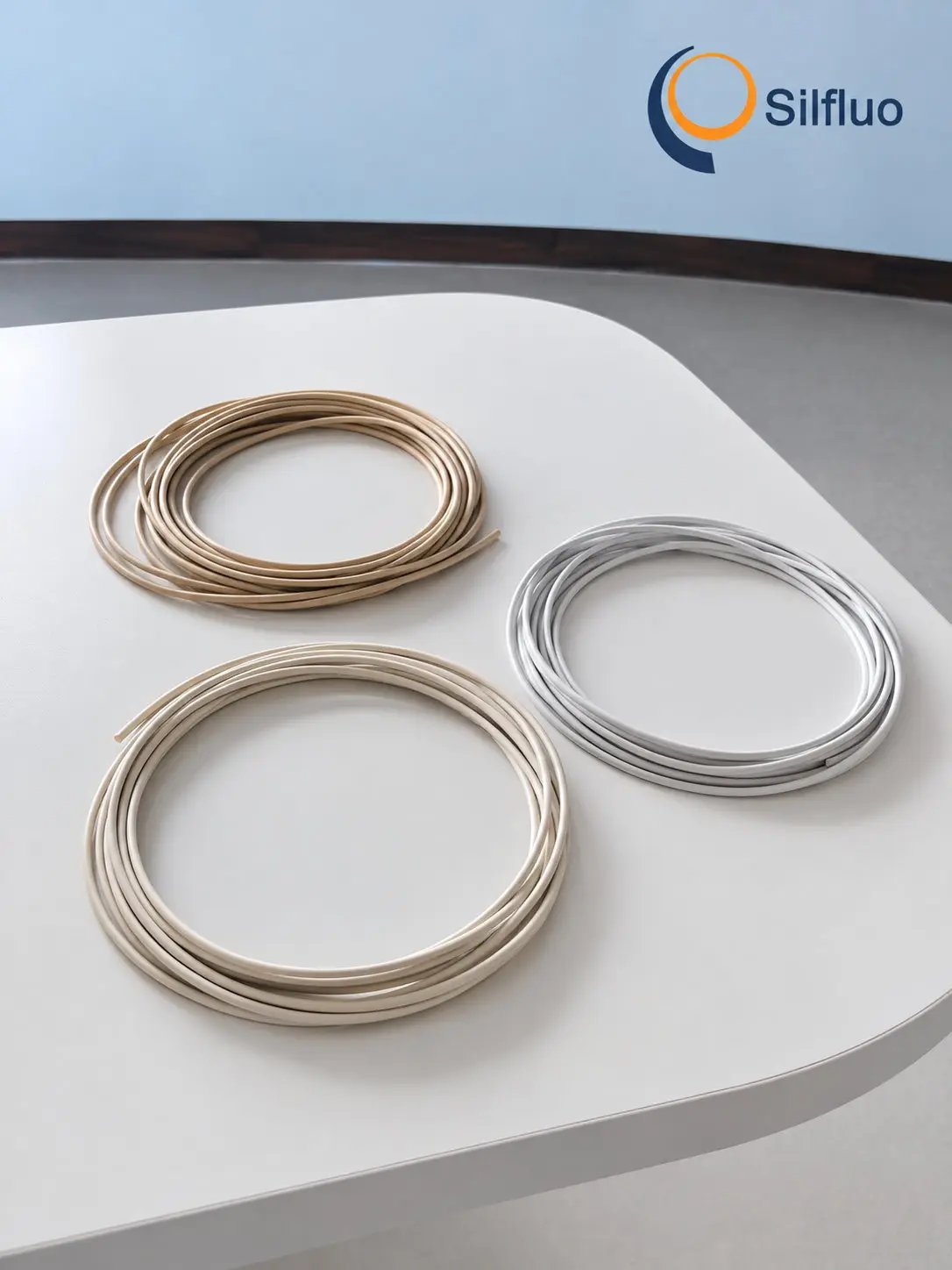 Three coils of wire finished with silazane insulating coating in tan, cream and grey, laid on a white bench